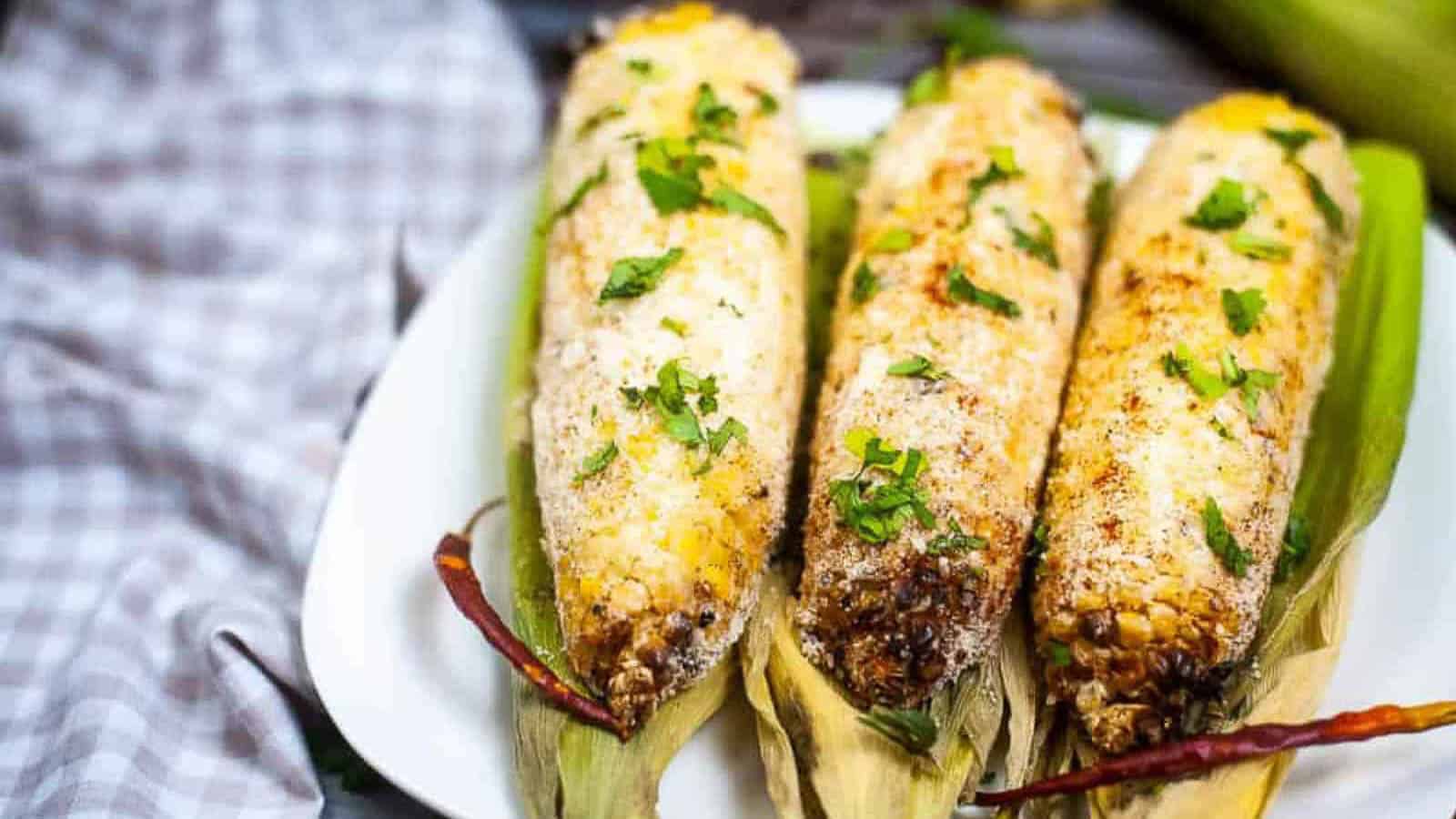 metal baking pan with elote, Mexican grilled corn cobs with mayonnaise, spices, and cheese.