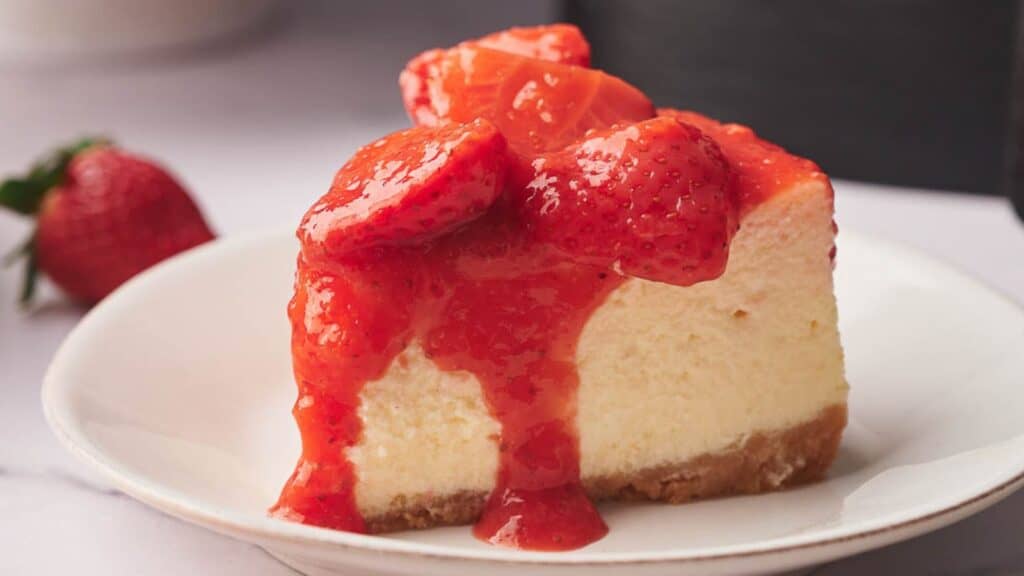 A slice of cheesecake with strawberry sauce on a plate.