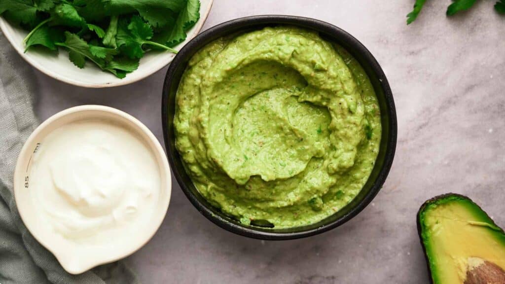 A bowl of avocado hummus and a bowl of sour cream.