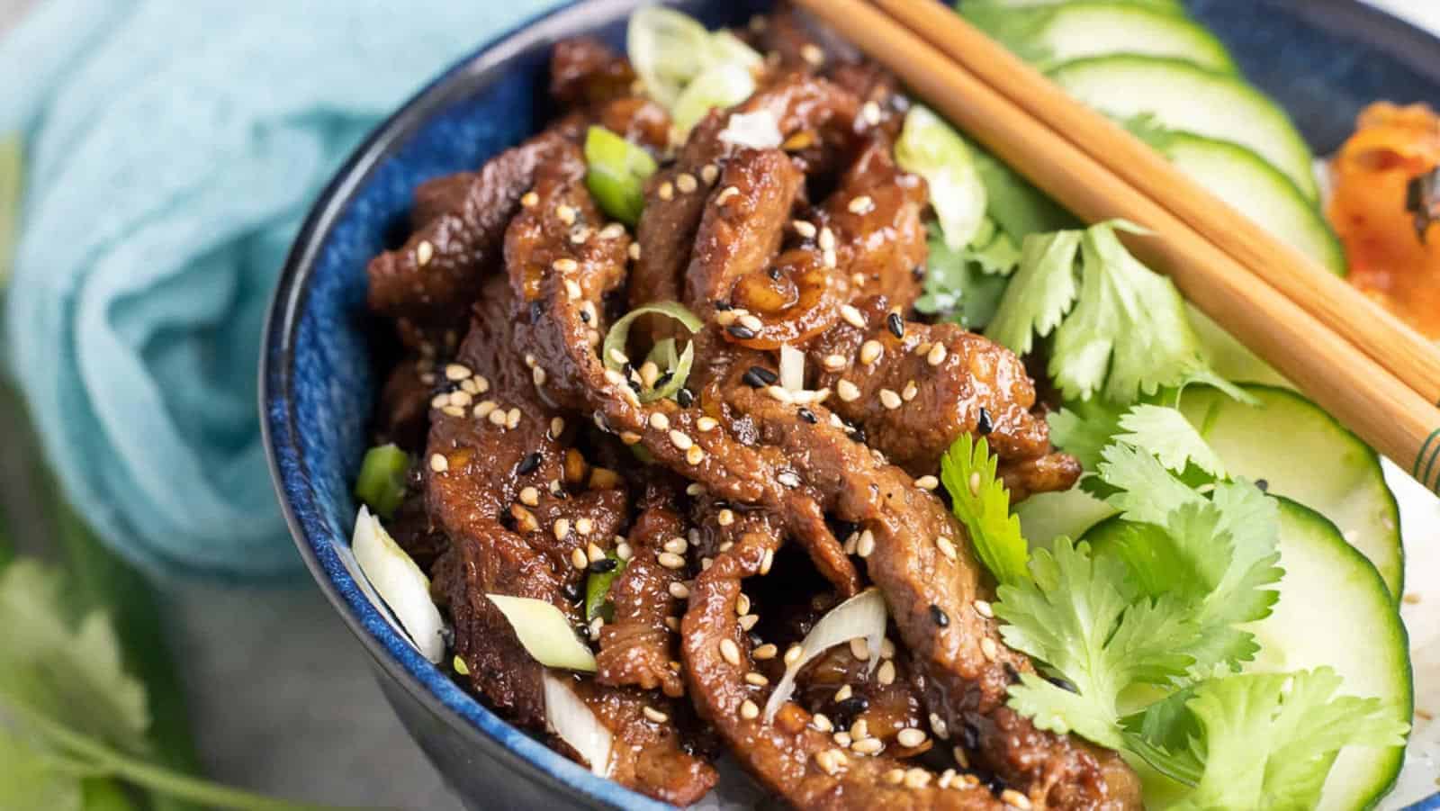 Beef bulgogi in a bowl with rice and cucumbers.