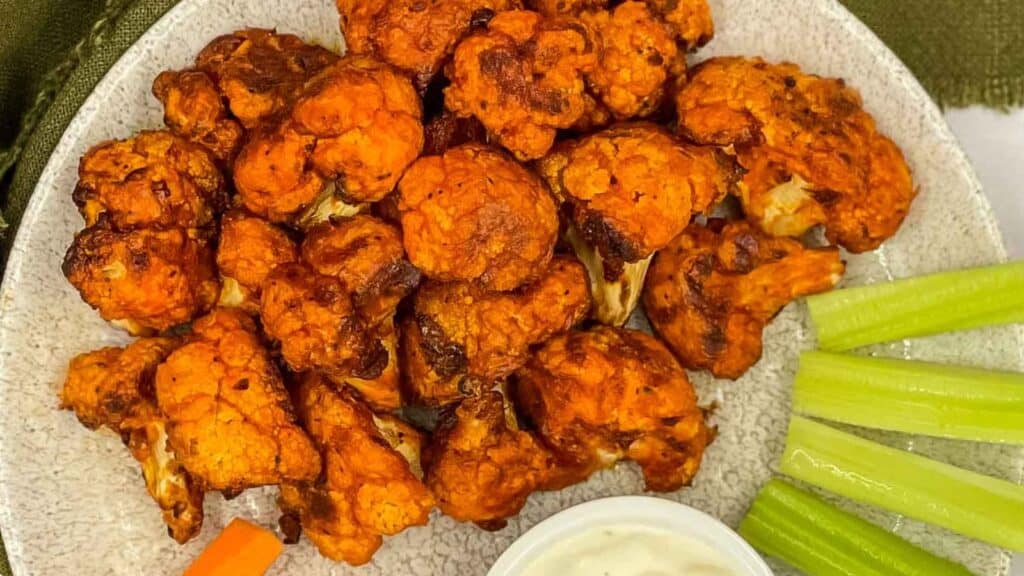 Buffalo cauliflower wings on a plate with celery and dipping sauce.