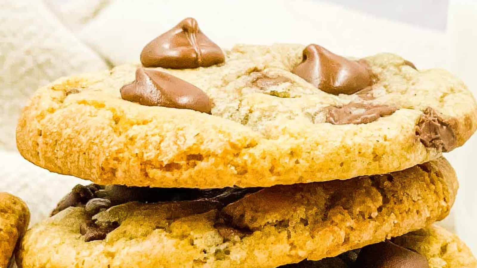 A hand holding a chocolate chip cookie on a cooling rack.