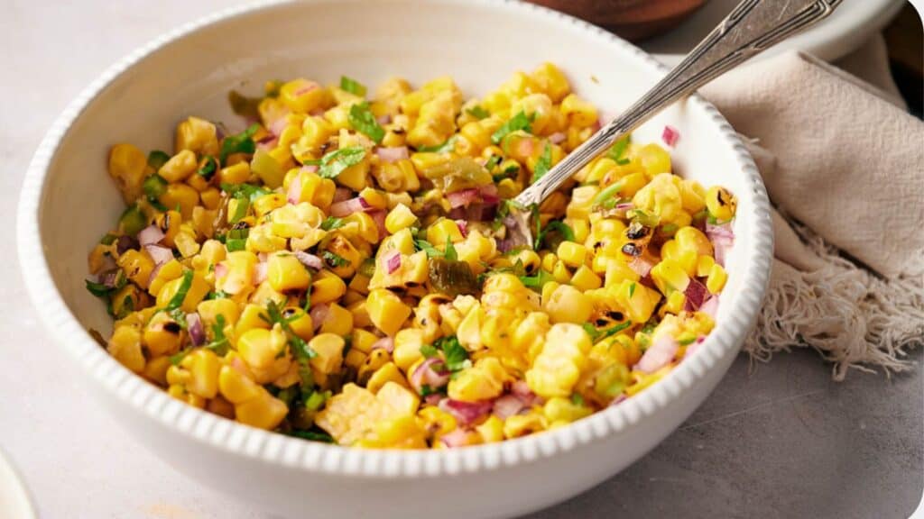 Corn salad in a white bowl with a spoon.