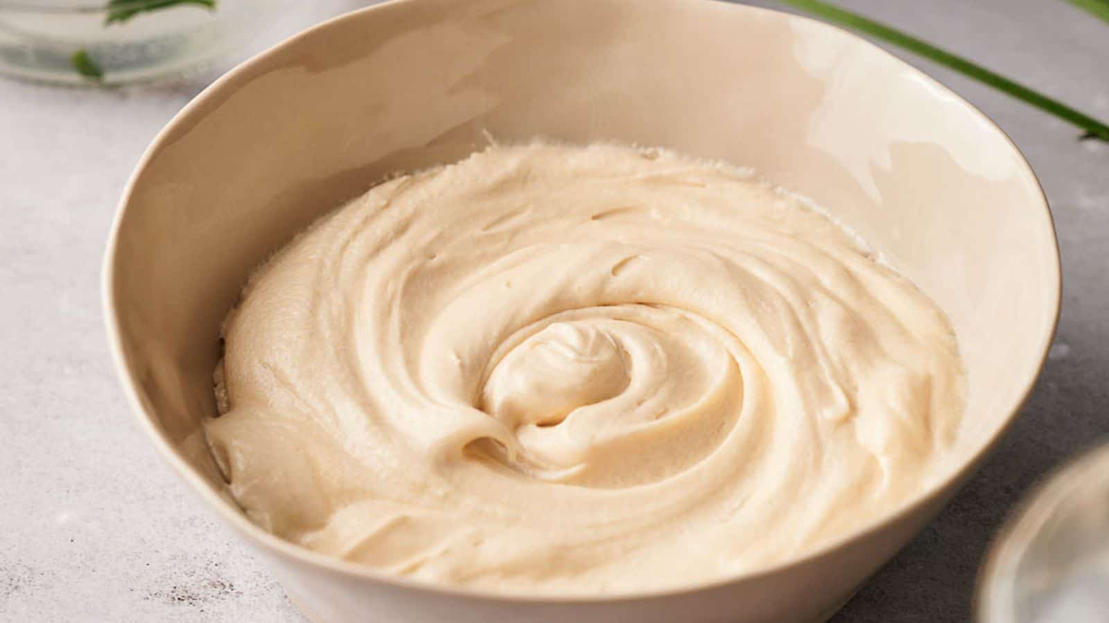 Cream cheese frosting in a bowl next to a glass of water.