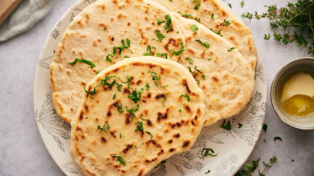 Naan bread on a plate with herbs and butter.