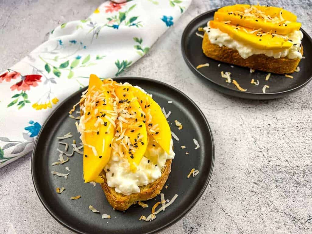 Two slices of Cottage Cheese Toast with Mango on round black plates.