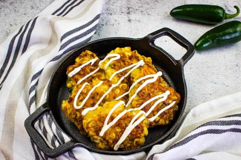 A skillet filled with Corn Fritters topped with a white sauce.