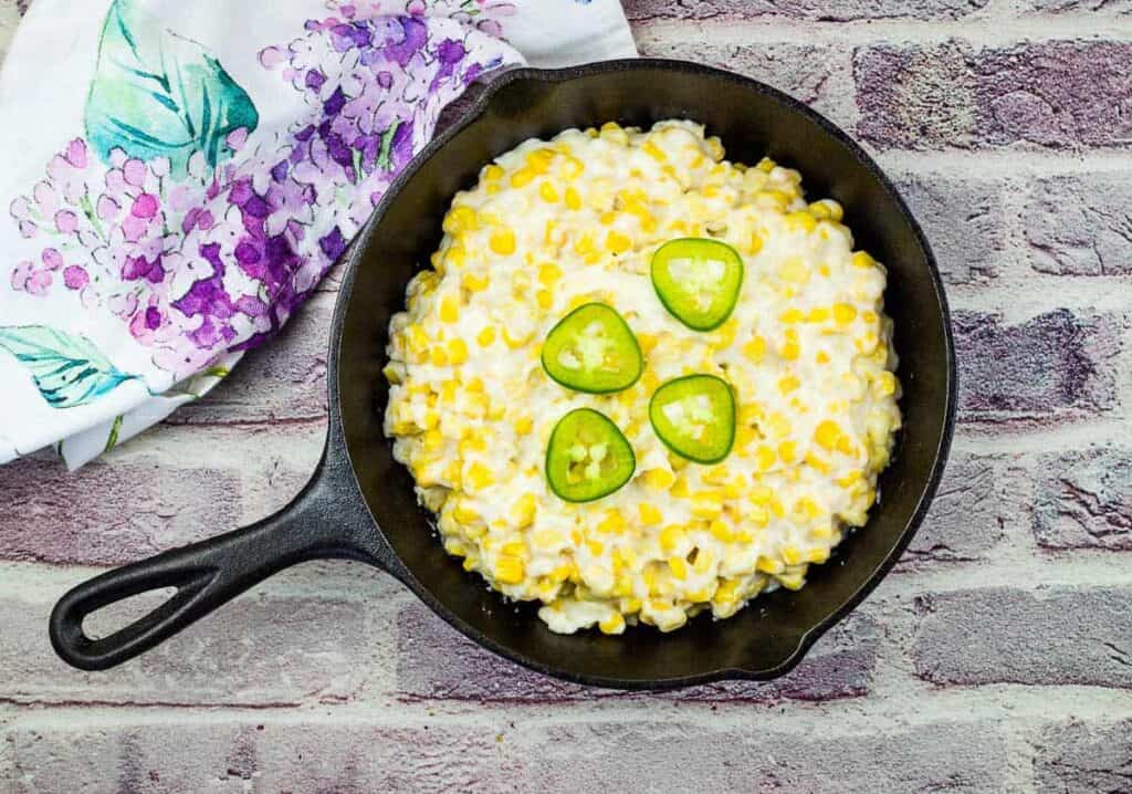 Creamed Corn in a skillet with jalapenos as a garnish.