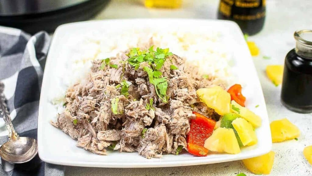 Instant pot pulled pork on a plate with rice and pineapples.