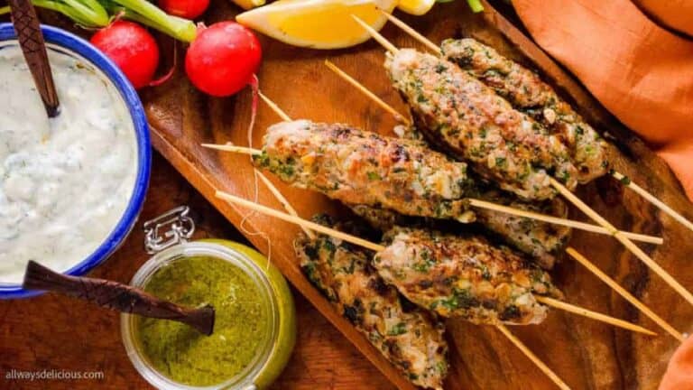 Lamb kofta kebabs on a wooden board with fresh herbs and vegetables.