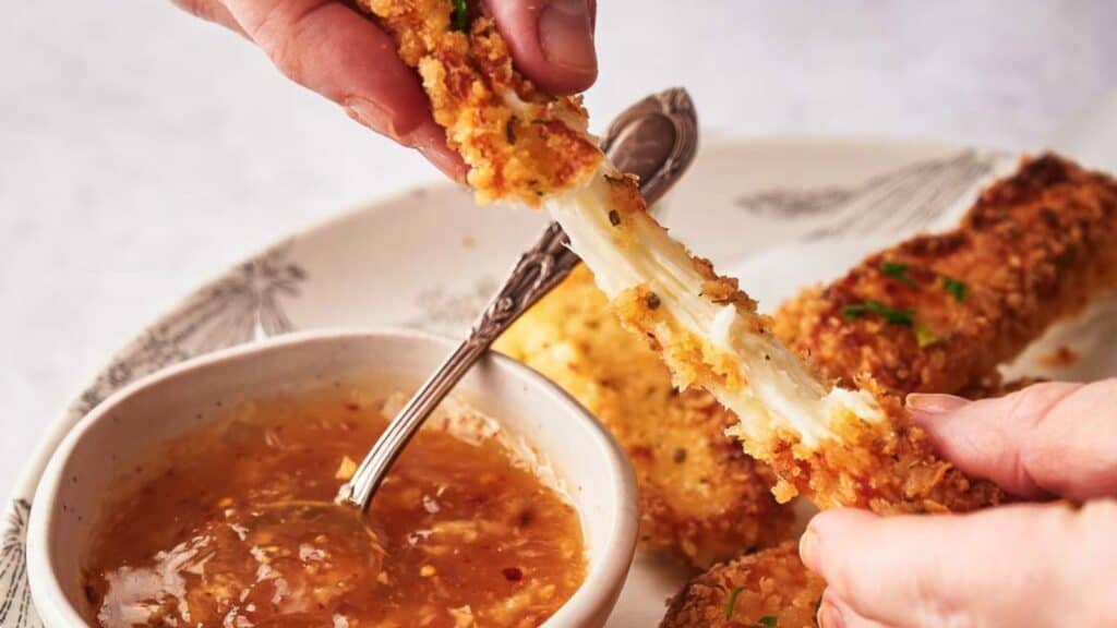 Someone pulling a mozzarella stick apart and showing the stretchy cheese.