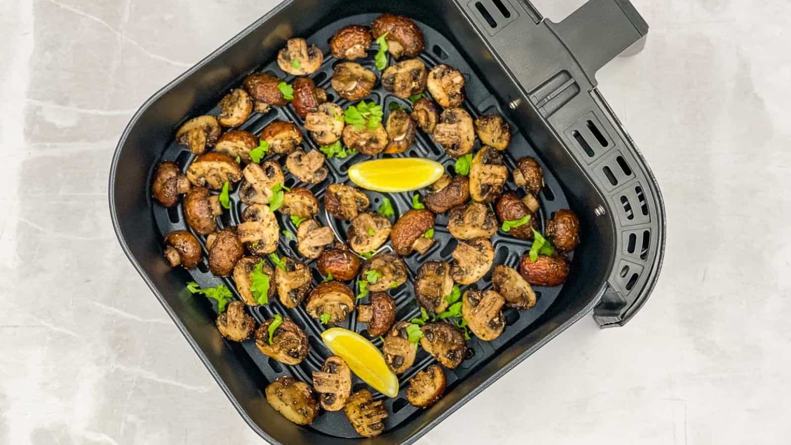 A air fryer basket filled with mushrooms and lemon wedges.
