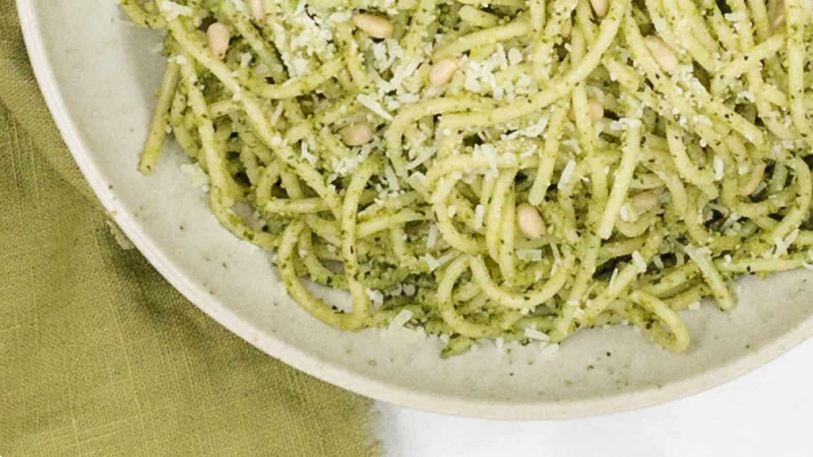 A bowl of pesto pasta with pine nuts and parmesan cheese.