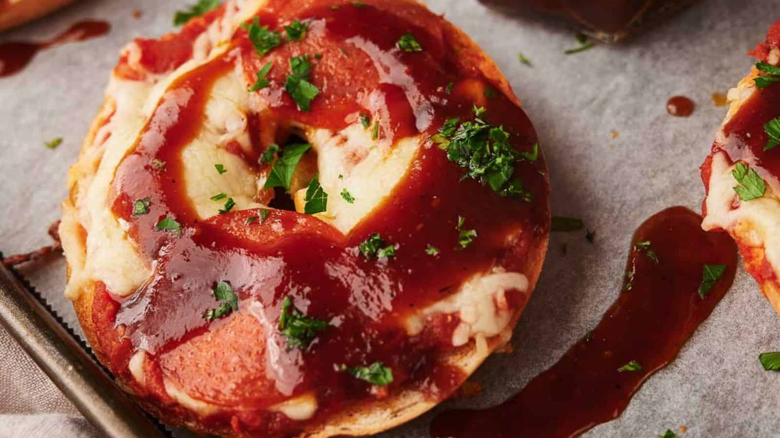 Pizza bagels on parchment paper, one with a bite out of it and a jar of BBQ sauce nearby.