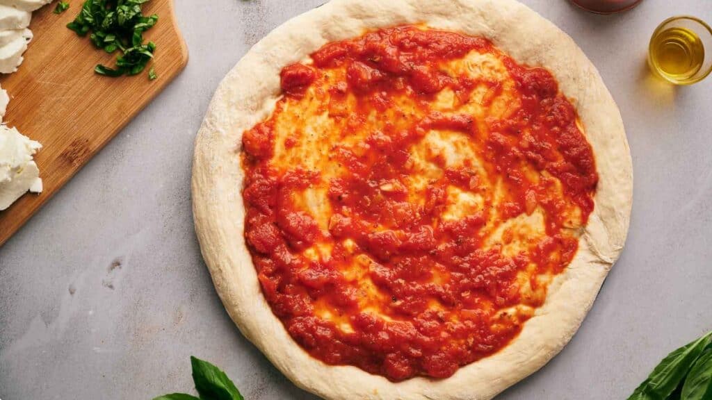 A pizza with tomato sauce and basil on a cutting board.