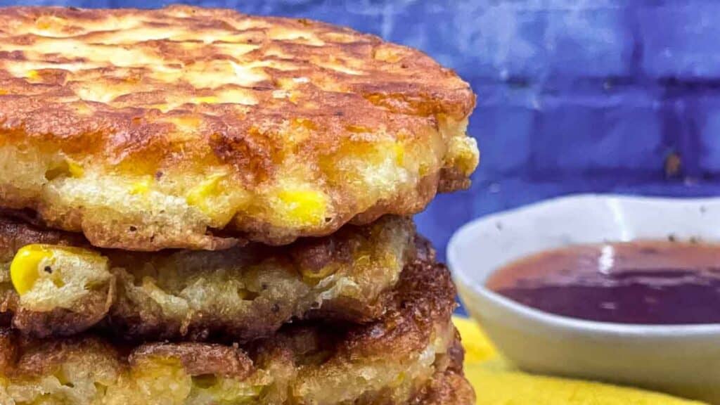 A stack of corn fritters next to a bowl of sauce.