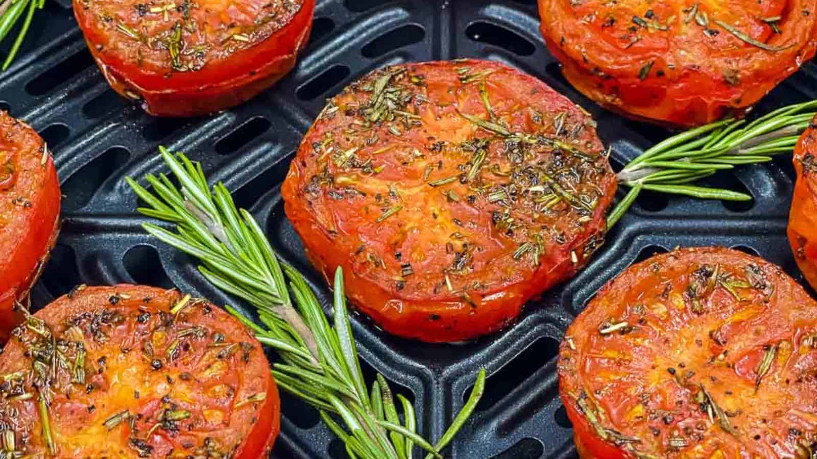 Air fried tomatoes in an air fryer basket with fresh rosemary.