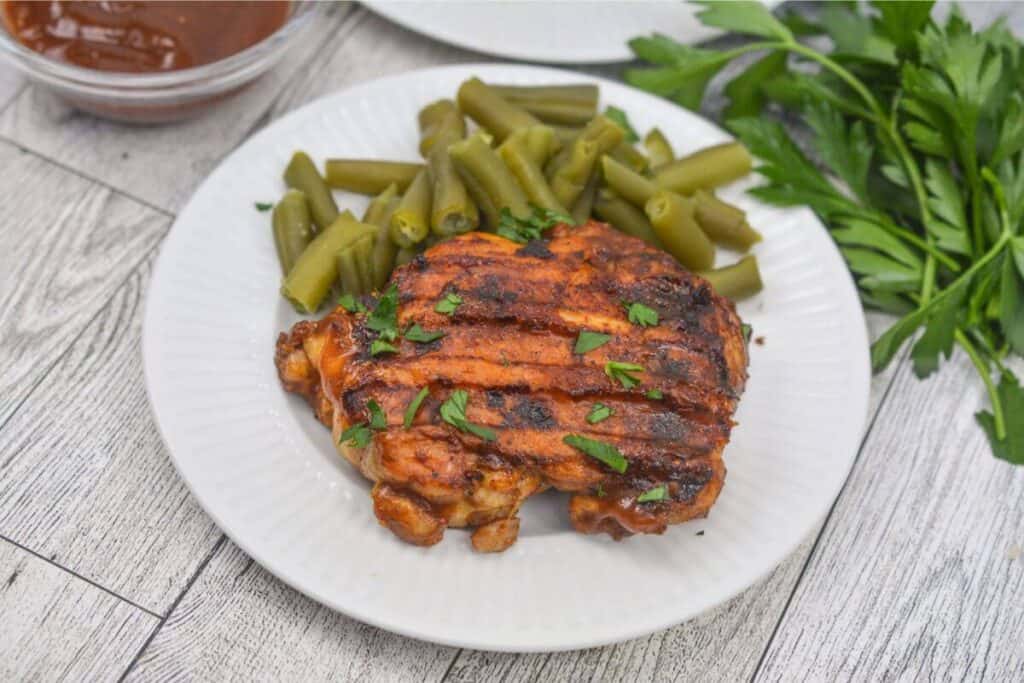 Bbq chicken with green beans on a white plate.
