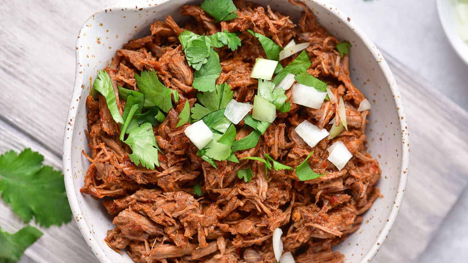 Overhead shot of a bowl of shredded beef birria with cilantro and chopped onions.