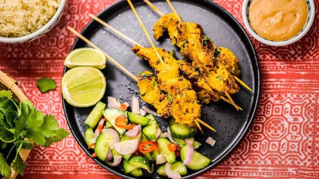 Thai chicken skewers on a plate with rice and vegetables.