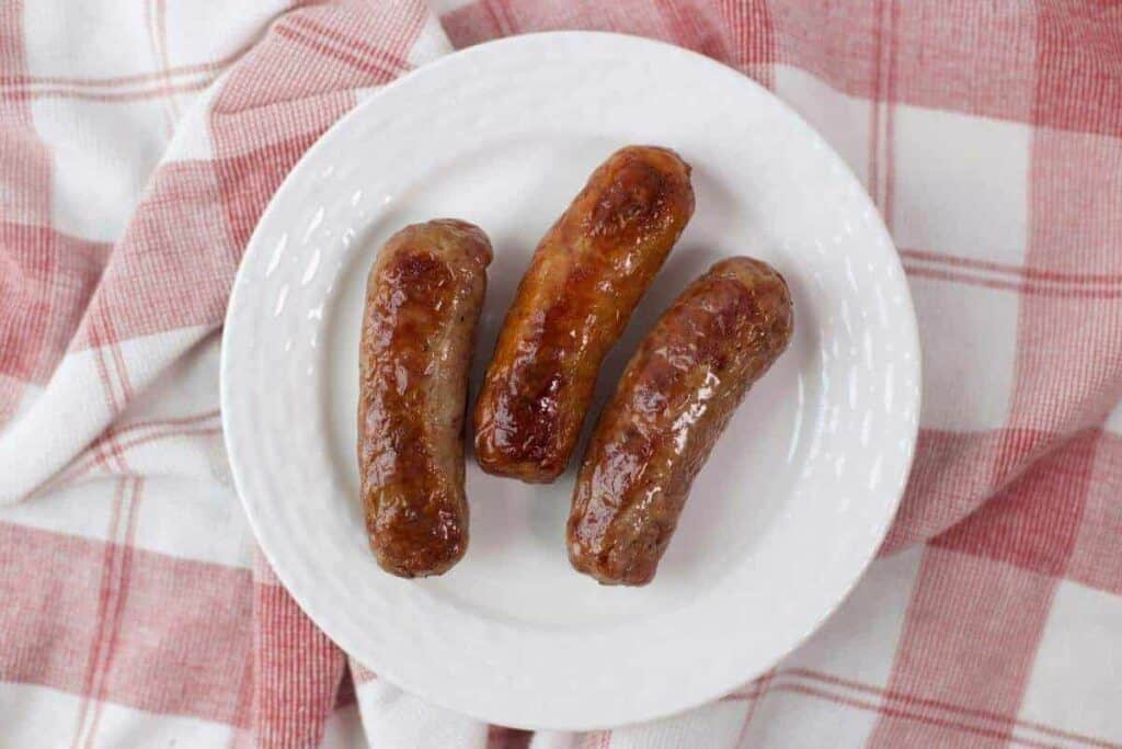 Three sausages on a plate on a red and white checkered cloth.