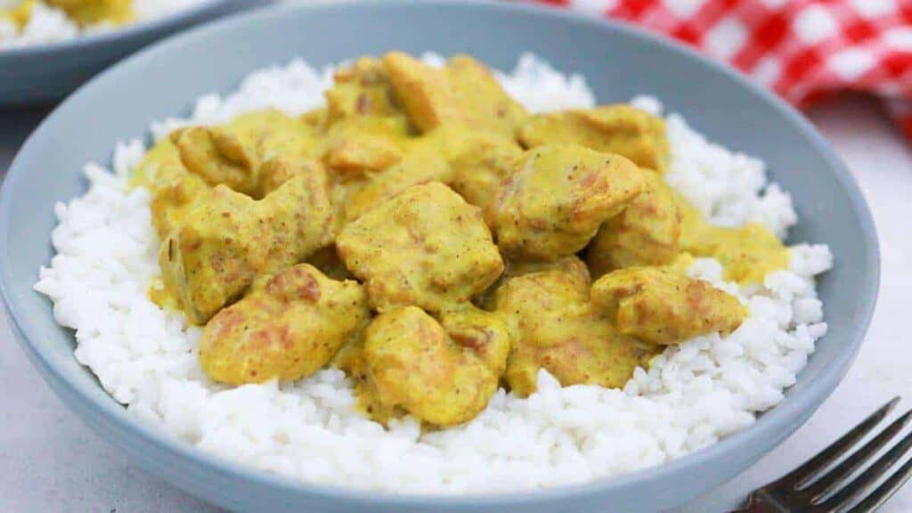 A bowl of chicken curry with rice and a fork.