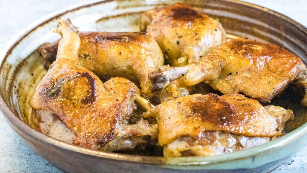 Chicken thighs in a brown bowl on a table.