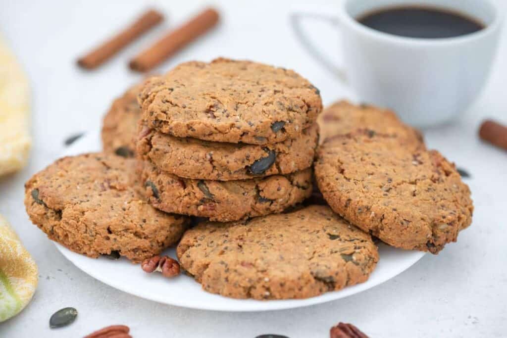 A stack of cookies on a plate next to a cup of coffee.