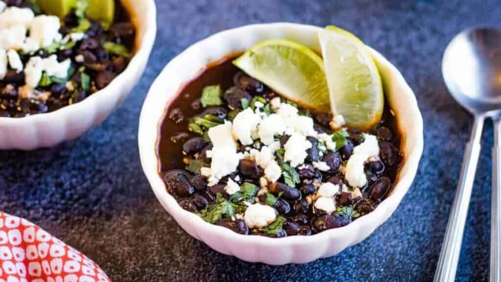 Two bowls of black bean soup with lime wedges.