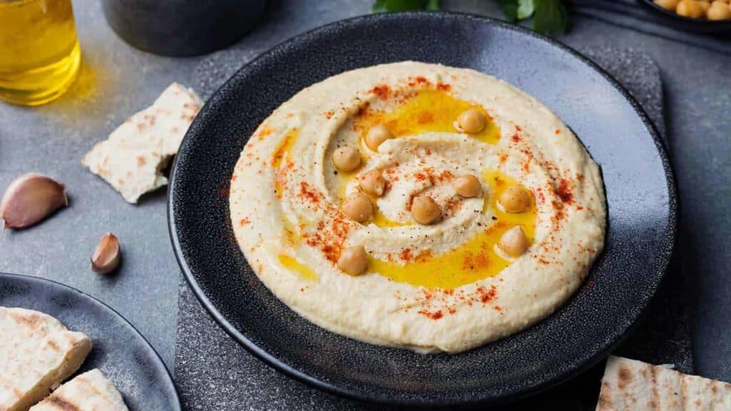 Hummus with chickpeas and pita bread on a black plate.