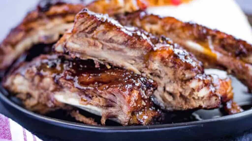 Bbq ribs on a black plate with a napkin.