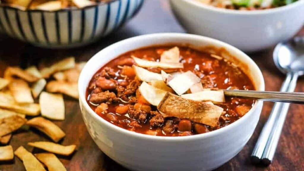 A bowl of chili with tortilla chips on a wooden table.