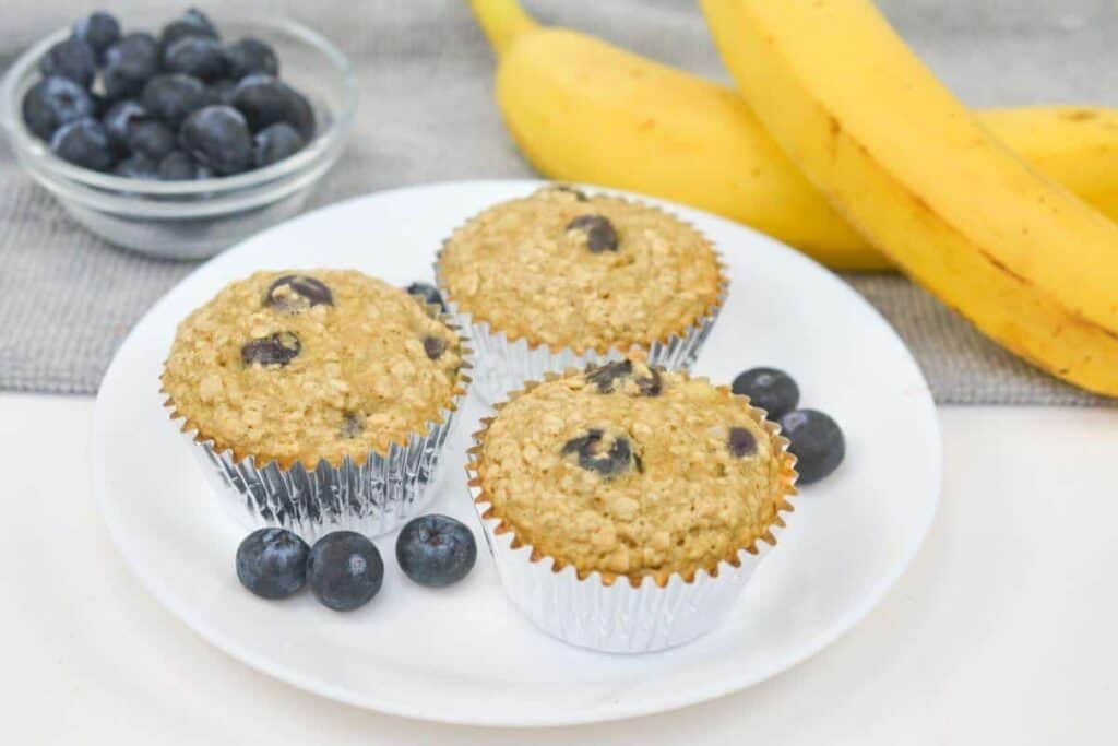 Blueberry muffins on a plate with bananas and blueberries.