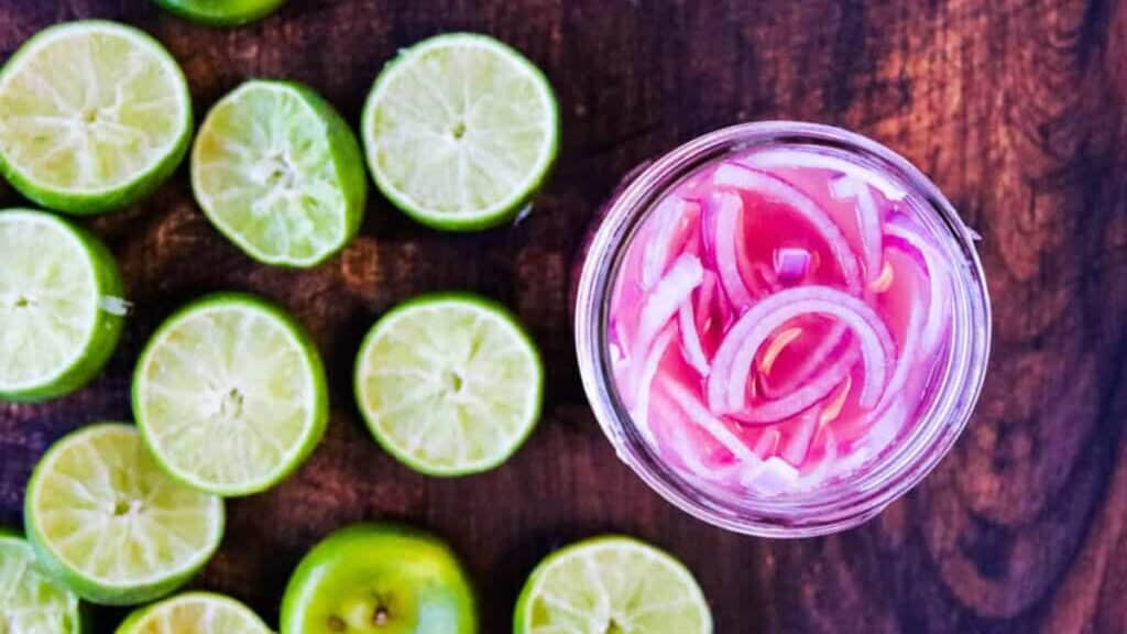 A jar of red onion and lime slices, perfect for taco recipes, on a wooden table.