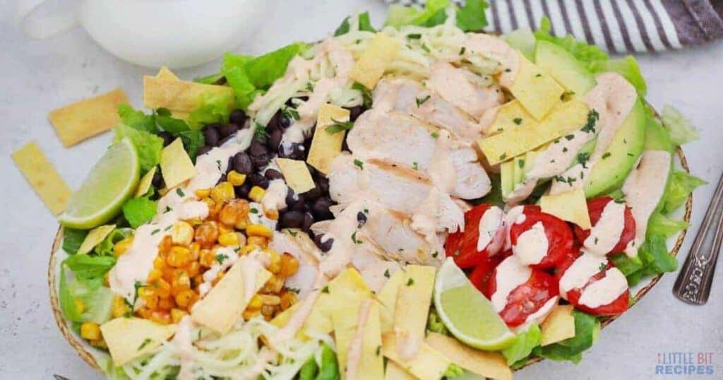 A salad with chicken, corn, tomatoes, and avocados on a plate.