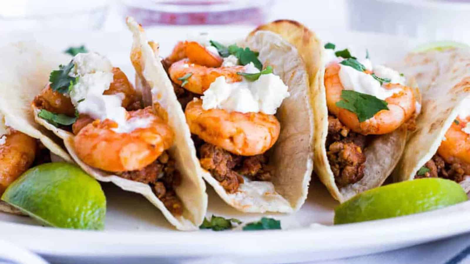 Shrimp tacos on a plate with lime wedges.