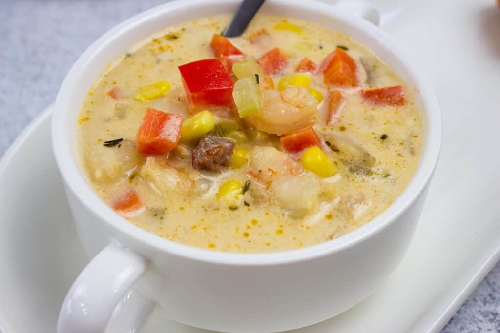 A bowl of chowder with shrimp and vegetables on a plate.