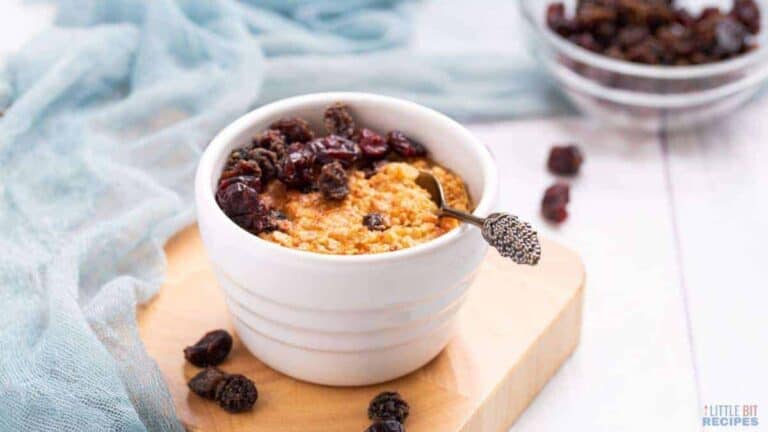 A cup of oatmeal with raisins and a spoon.