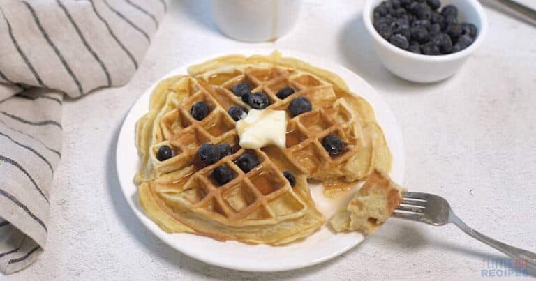Waffles with butter and blueberries on a plate.