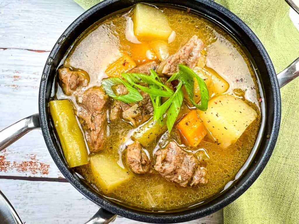 A pot of soup with meat and vegetables on a wooden table.