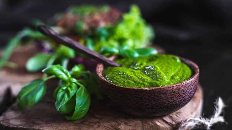 Bright green basil pesto inside a wooden bowl.