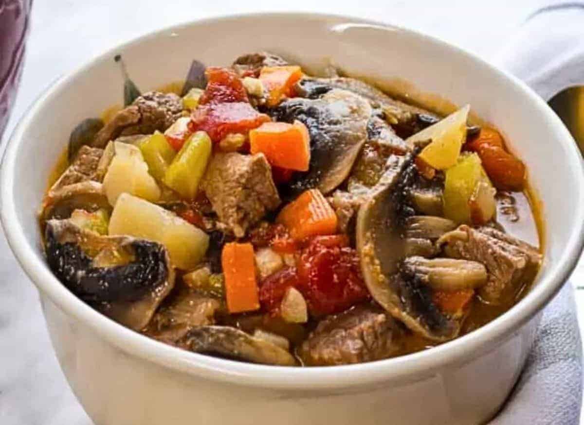 A bowl of beef stew with vegetables and mushrooms.
