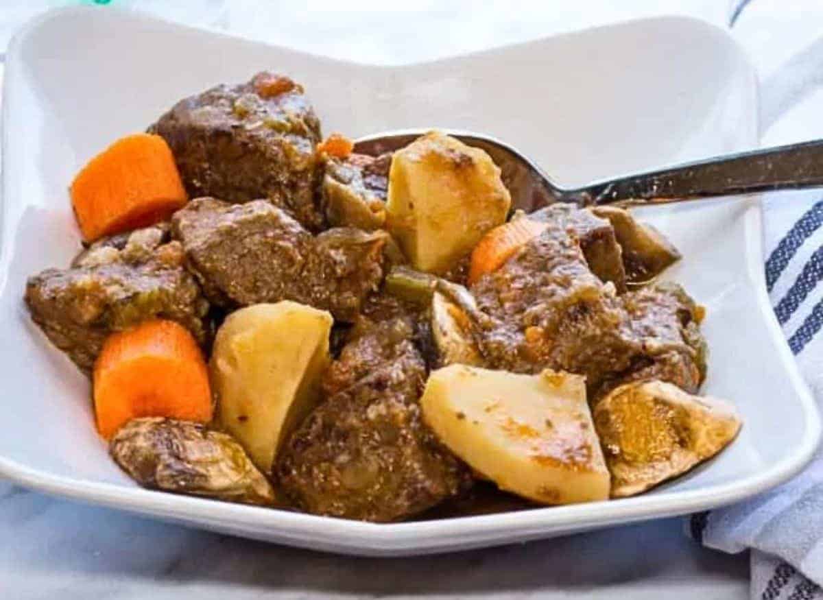 Beef stew in a white bowl with carrots and potatoes.