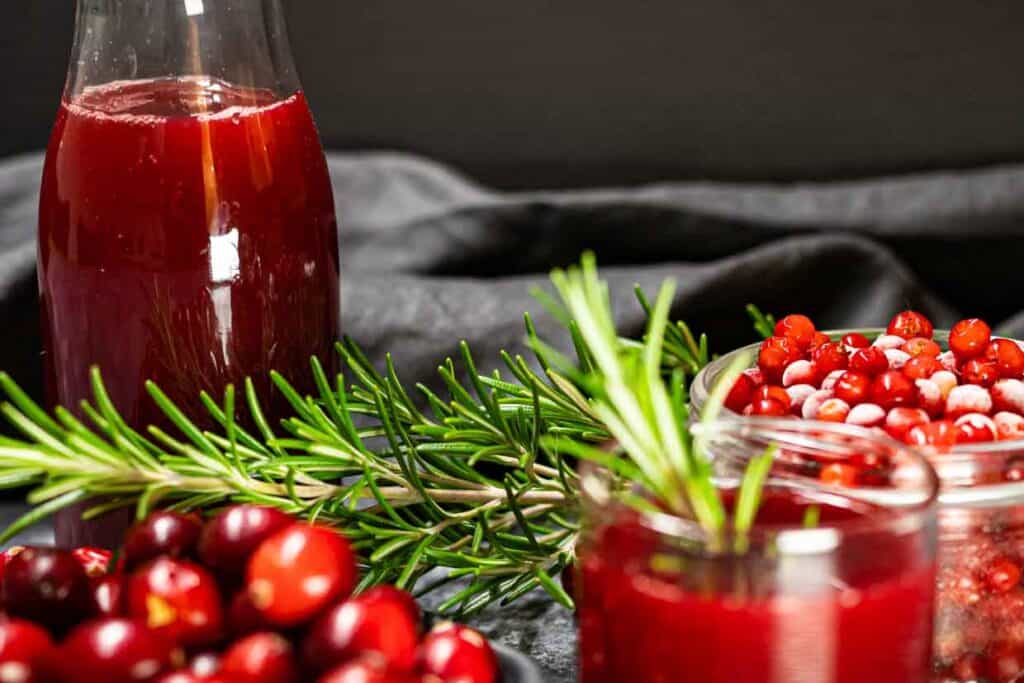 A bottle of cranberry juice with cranberries and rosemary.