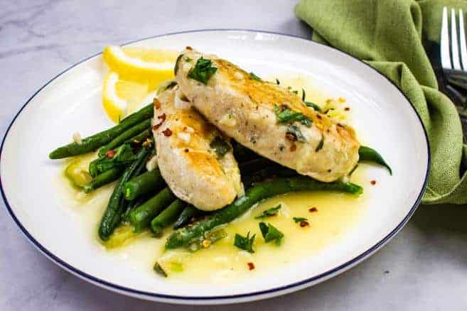 A white plate with Chicken Scampi and green beans resting in the center.