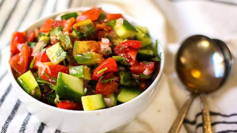 Kachumber salad in a white bowl with fancy silver spoons on the side.