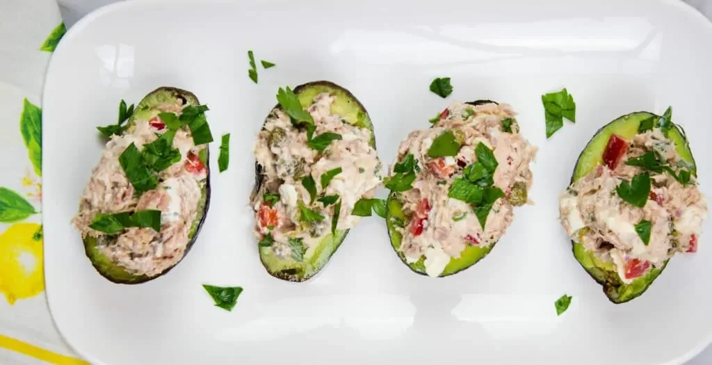 Four Mediterranean Tuna Salad stuffed avocados on a white plate.
