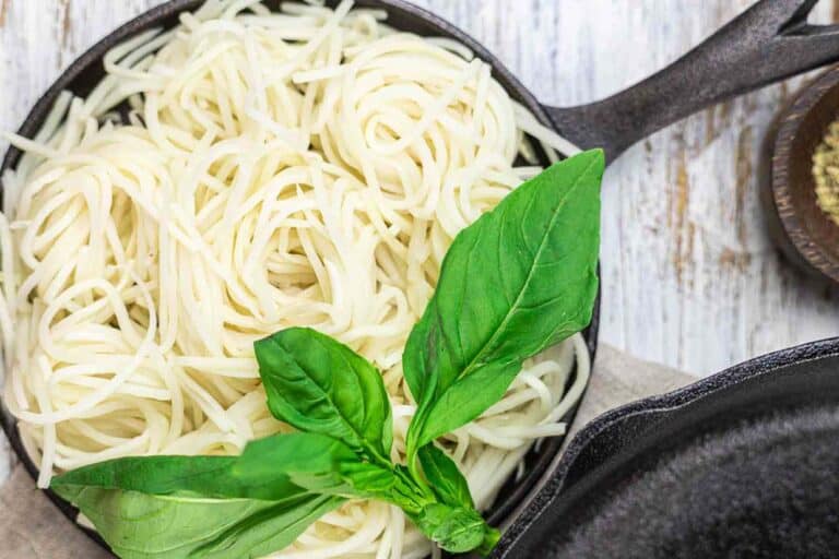 Pasta in a skillet with basil leaves.
