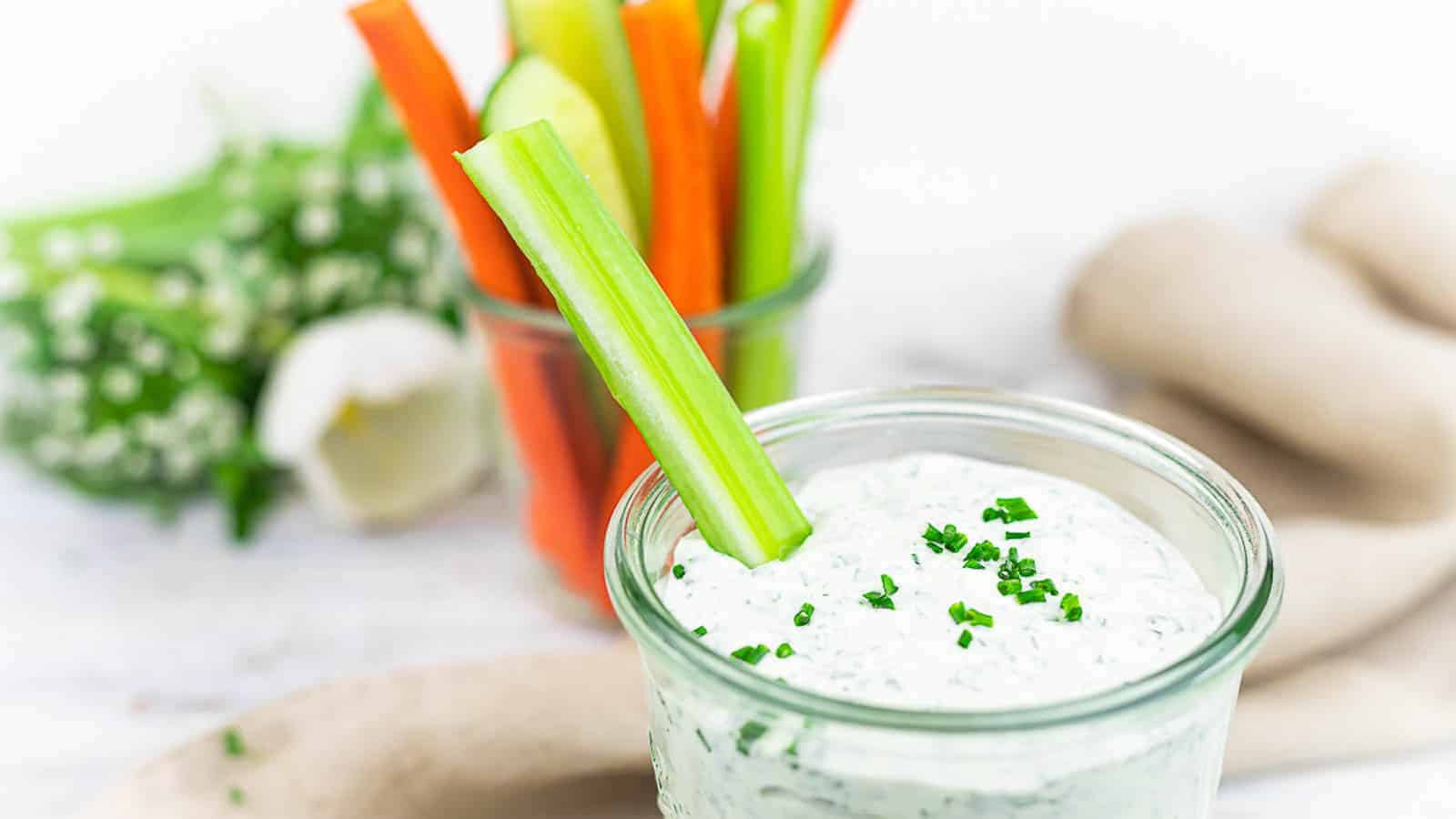 Ranch dressing in a glass bowl with sticks of veggies. 