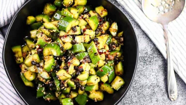 Overhead shot of spicy cucumber salad in a black bowl with a fancy serving spoon on the side.